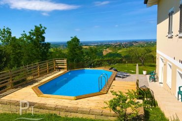 Piscina fuori terra Jardin 814 con bordo in legno naturale, incastonata in un giardino con vista sulle colline, per momenti di puro relax all’aperto.