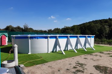 Piscina fuori terra GRE Atlantis 915x470 in acciaio bianco, dotata di tiranti diagonali e liner azzurro, è stata installata su un elegante prato sintetico.